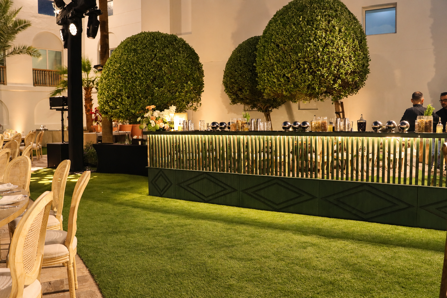 Illuminated modular bar with garnishes and glassware in a landscaped outdoor event setting