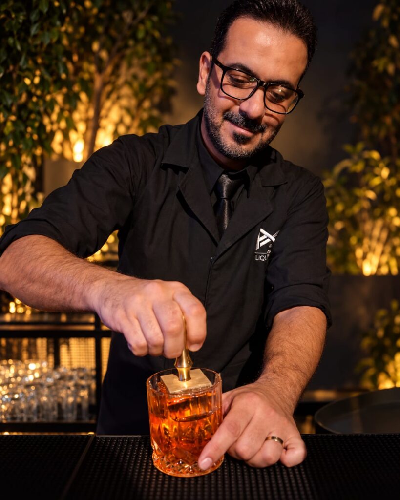 Tareq in glasses stamping a large ice cube in an amber cocktail