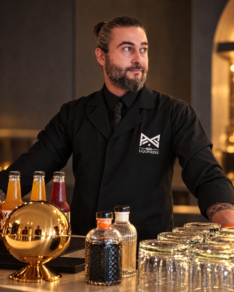 Tareq, Leading Mixologist, standing behind a bar in a black LiquiNeers uniform