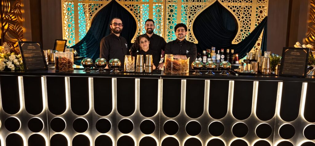 Four LiquiNeers team members behind an illuminated black bar with a gold geometric backdrop
