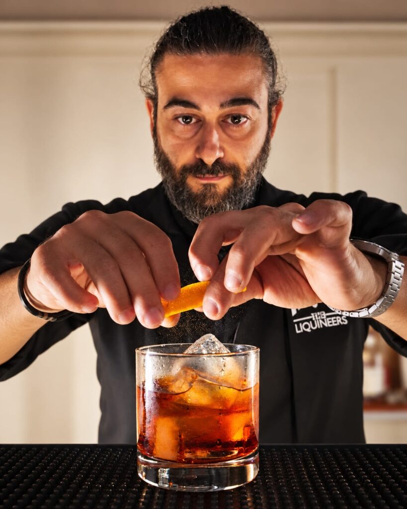 Tareq expressing orange peel over an amber cocktail