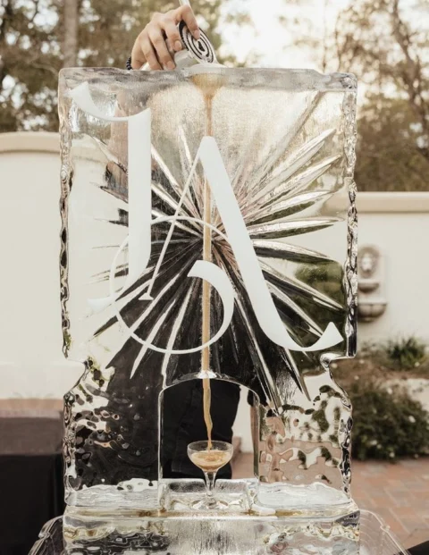 A drink poured through a monogrammed ice luge into a coupe glass at an outdoor event.