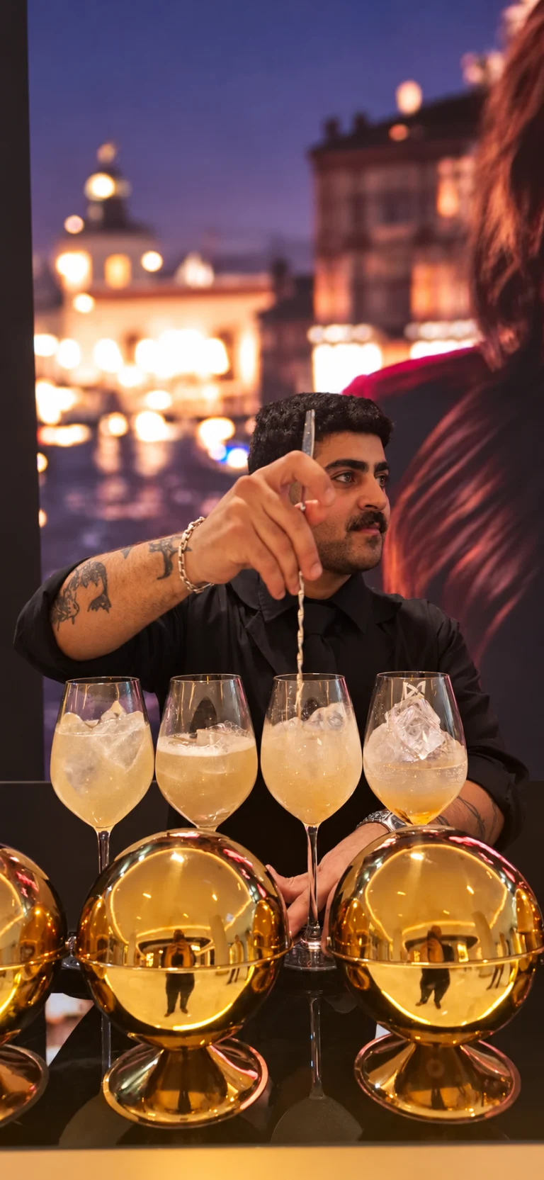 Riza stirring drinks behind The LiquiNeers bar with gold bar accessories