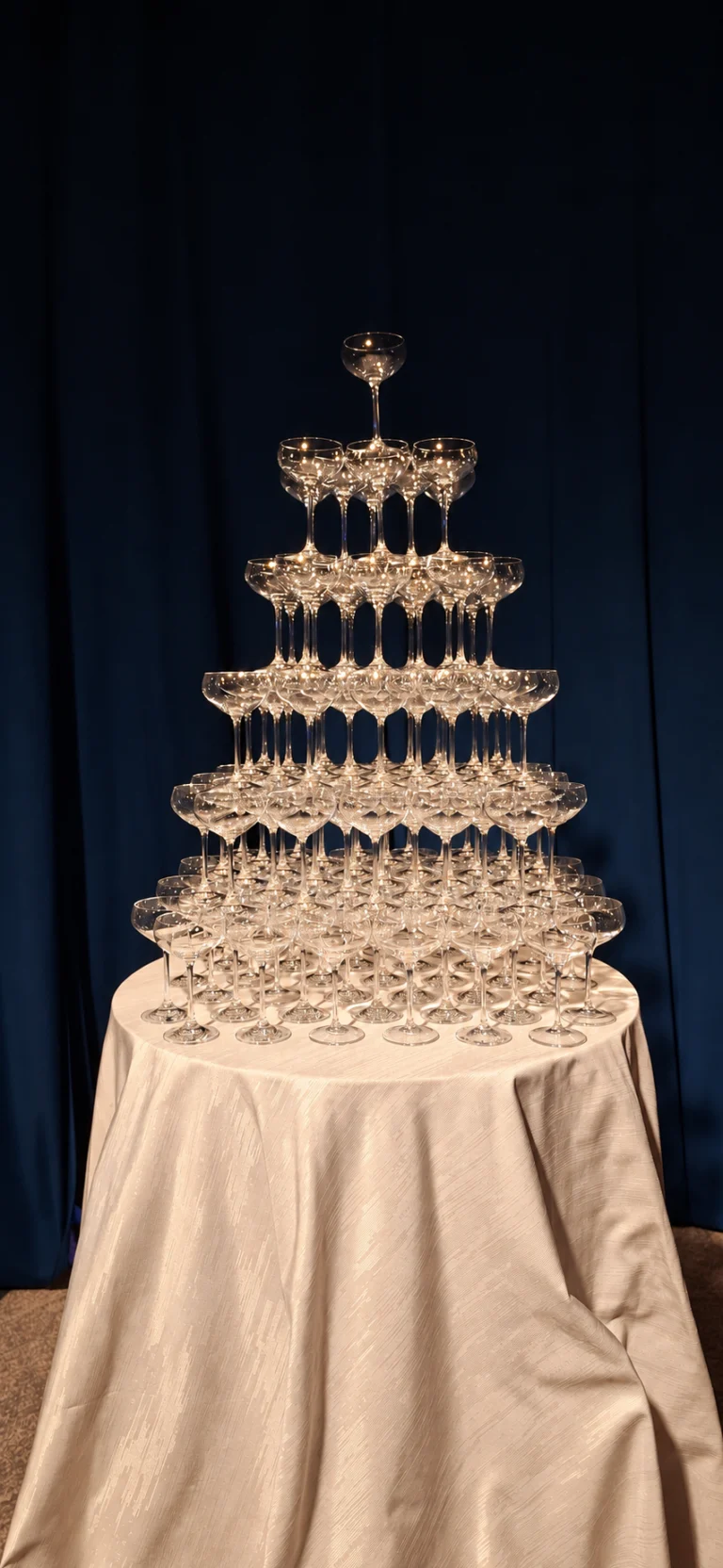 Tiered champagne coupe tower on a draped table against dark curtains