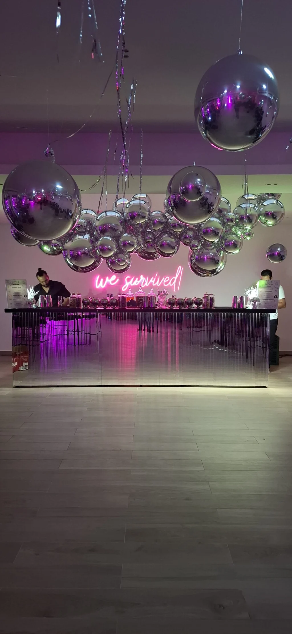 Mirrored event bar with mixologists, silver hanging balloons and a pink neon sign