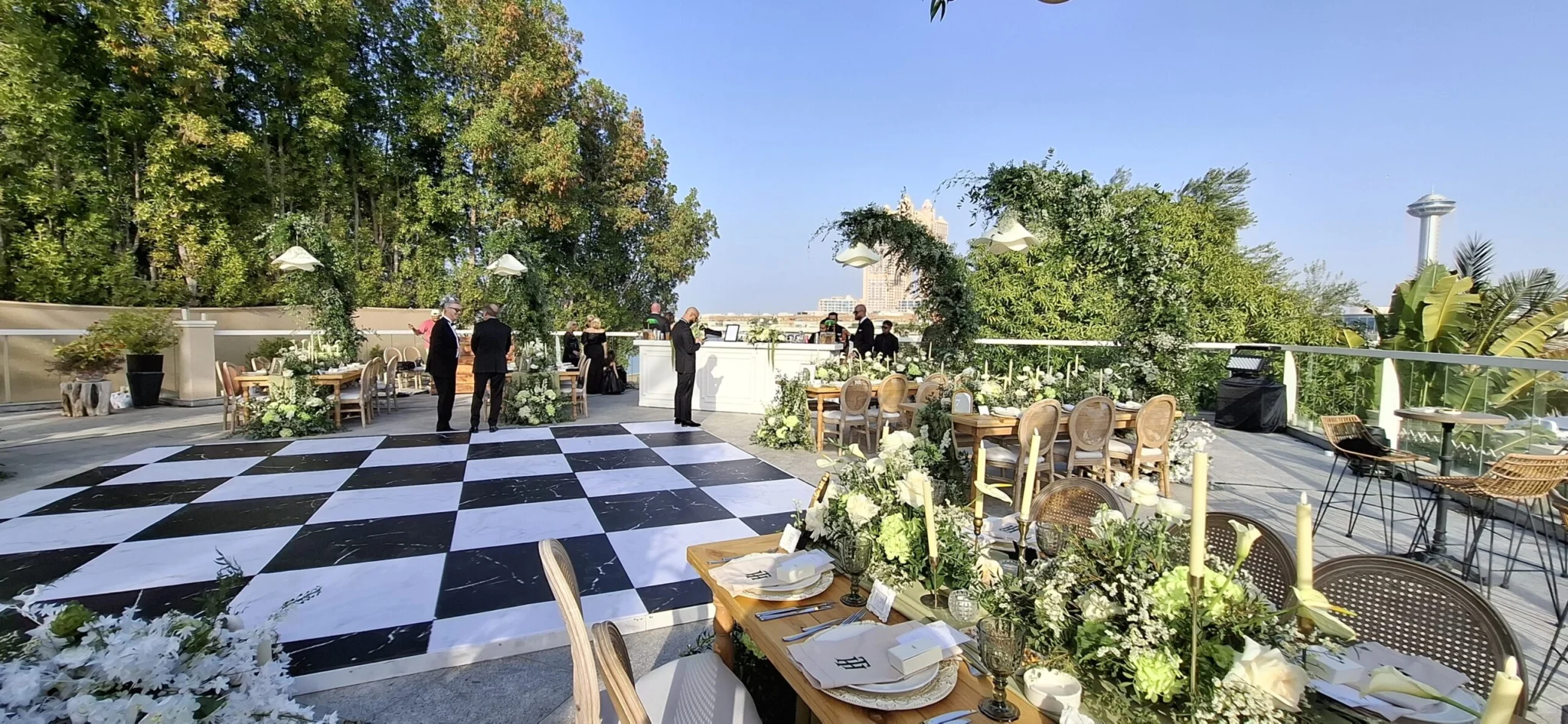 Outdoor reception with a white bar, floral dining tables and a black-and-white dance floor